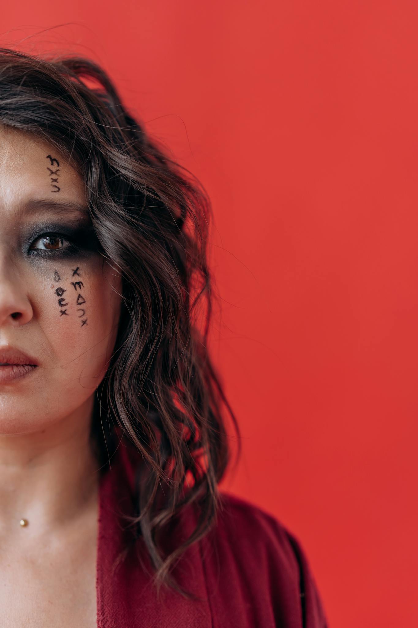 Dramatic portrait of a woman with artistic face paint and bold makeup against a striking red backdrop.