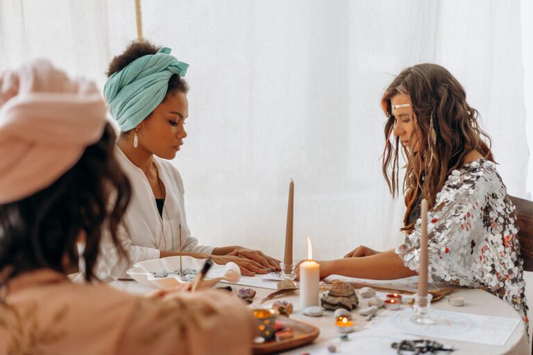 Three women engaging in a spiritual meditation session indoors with candles and crystals.