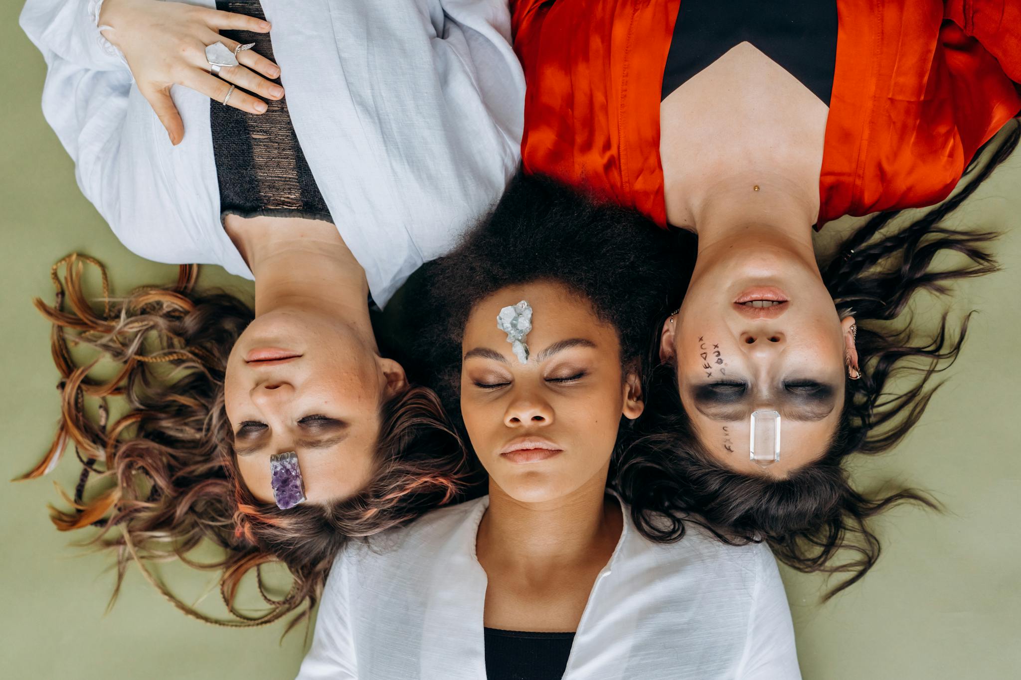 Three women lying on a mat with crystals on their foreheads, practicing mindfulness.